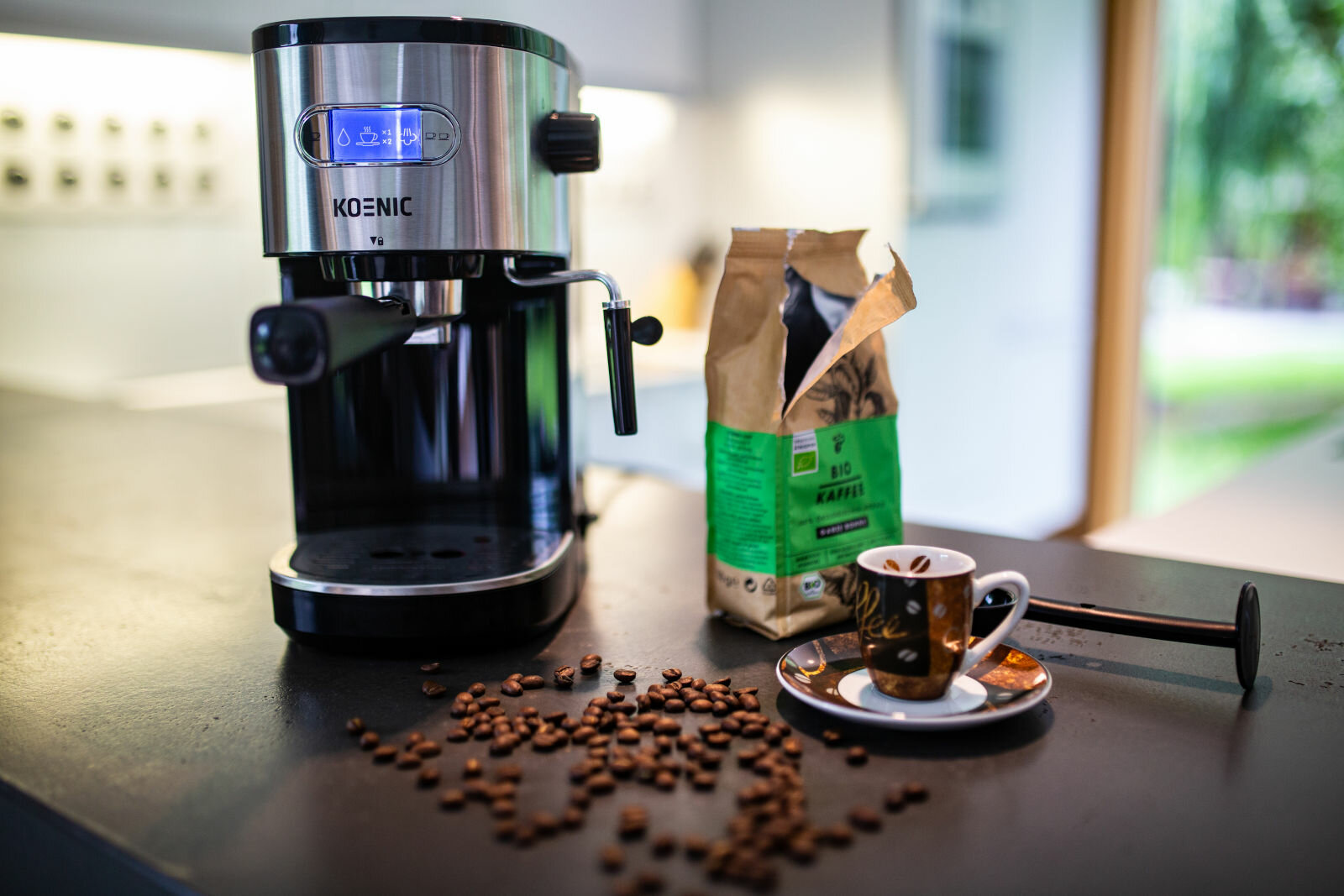 Ekspres do kawy z ziarnami kawy i filiżanką na ciemnej powierzchni w kuchni.