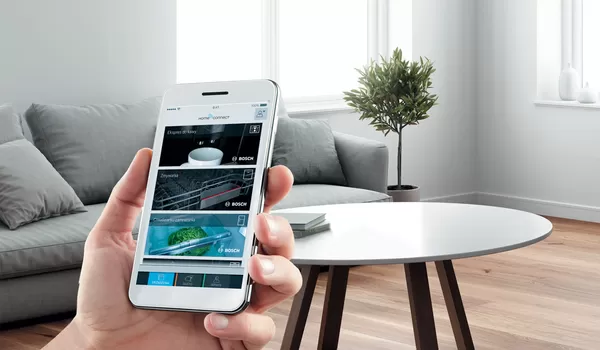 Osoba trzymająca smartfon z interfejsem aplikacji Bosch Home Connect w salonie.