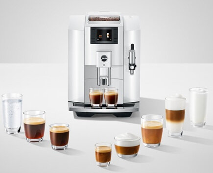 Biały ekspres do kawy z napojami kawowymi i szklankami wody.