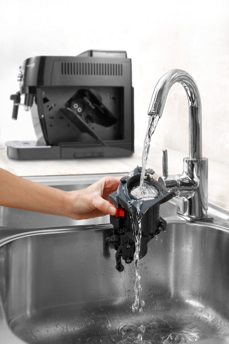 Osoba myje część ekspresu do kawy pod chromowaną baterią w zlewie ze stali nierdzewnej.