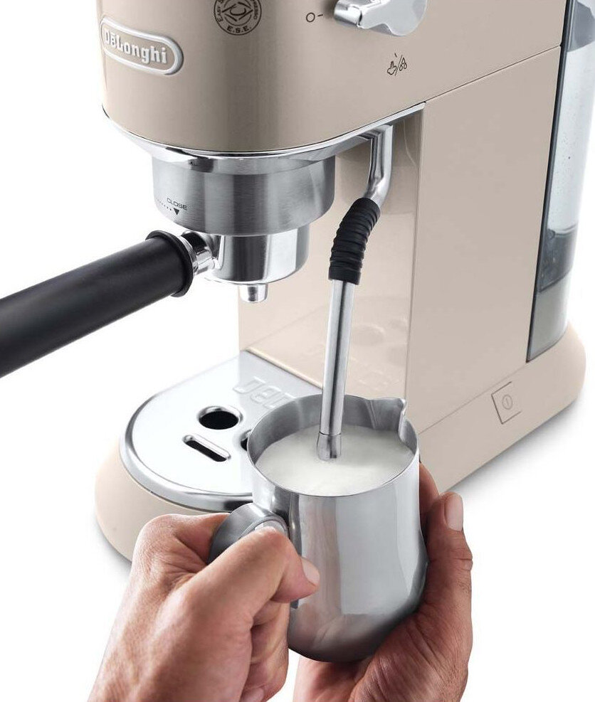 Beżowy ekspres do kawy spieniający mleko w metalowym dzbanku, czyjaś dłoń go trzyma.