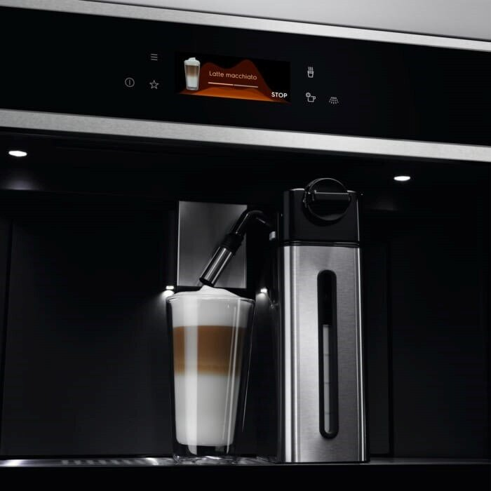 Ekspres do kawy robiący latte macchiato. Szklanka z warstwami mleka i kawy, pojemnik ze stali nierdzewnej i ekran.