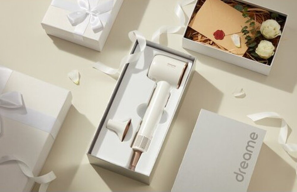 Zestaw upominkowy z białą suszarką do włosów w pudełku, otoczony innymi pudełkami prezentowymi i dekoracjami.