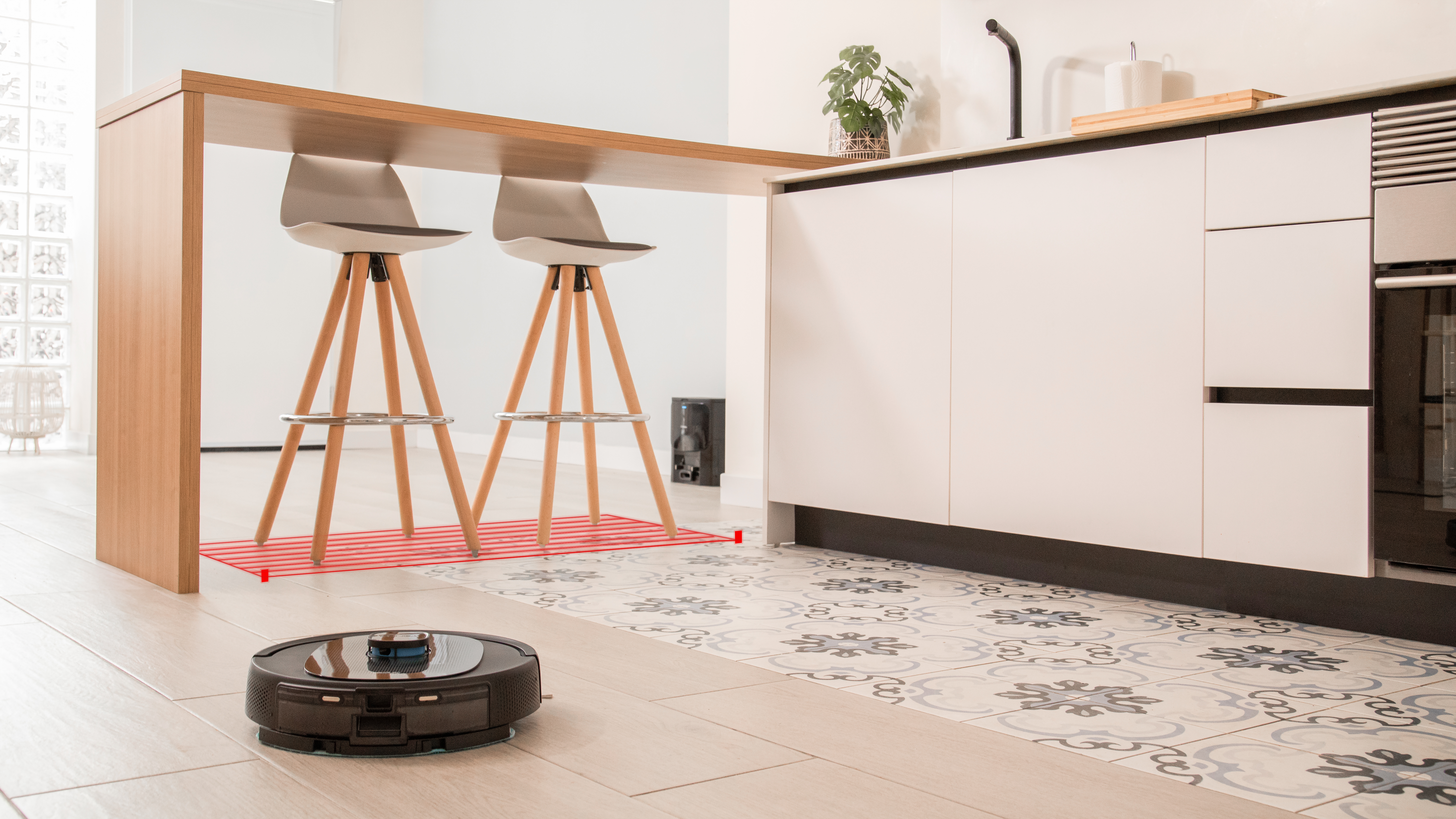 Una cocina con una isla de madera y dos taburetes. Una aspiradora robot está en el suelo.
