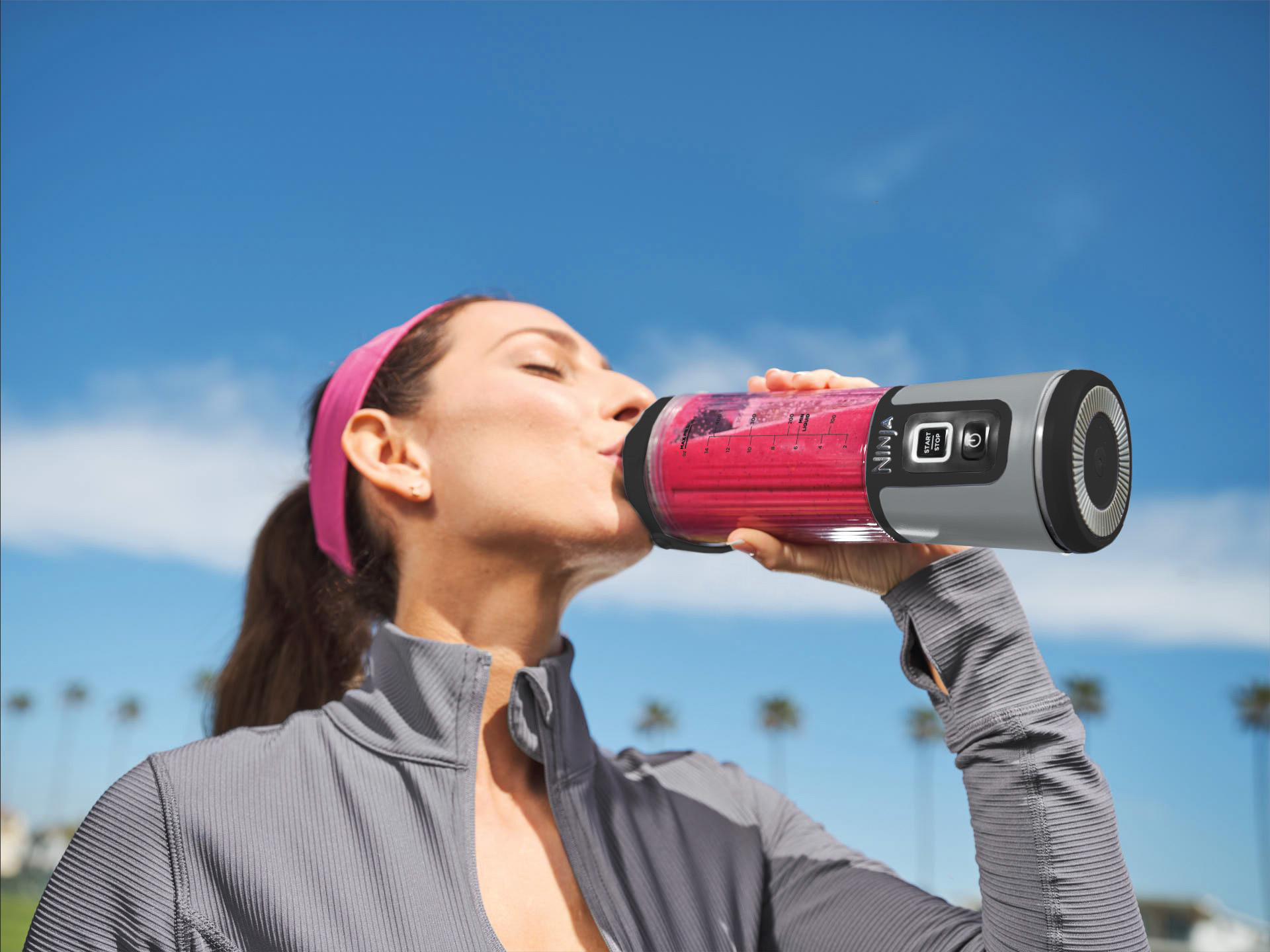 Eine Frau trinkt einen rosa Smoothie aus einer Mixerflasche im Freien.