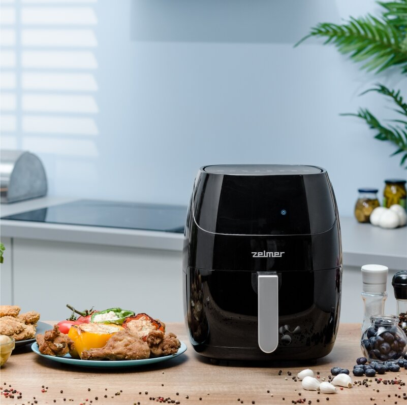 Czarna frytkownica powietrzna z jedzeniem z przodu. Smażony kurczak i warzywa na niebieskim talerzu.