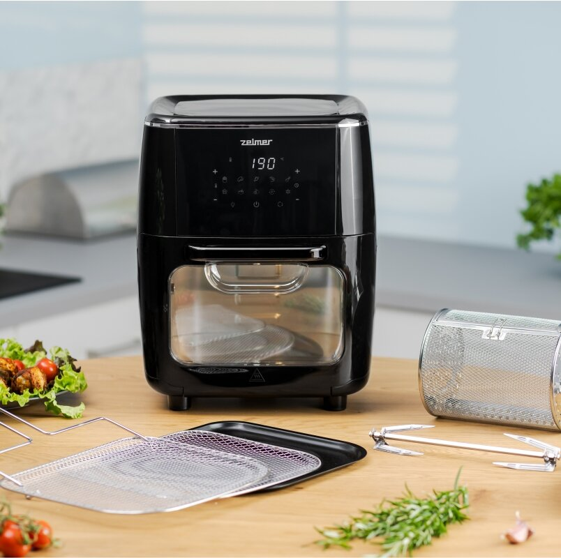 Czarna frytkownica na drewnianym stole z akcesoriami i jedzeniem, rozmyte tło kuchni.