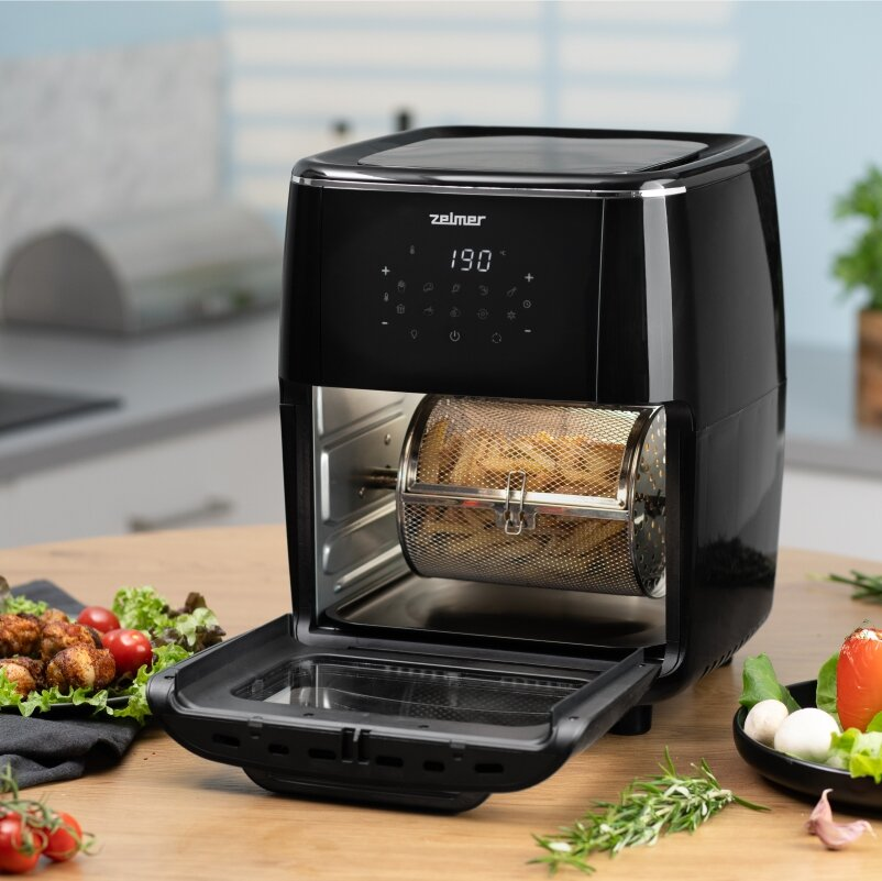 Czarna frytownica powietrzna z otwartymi drzwiami, pokazująca frytki. Warzywa są w pobliżu.