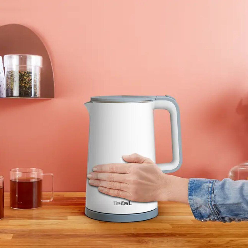 Biały i szary czajnik elektryczny na drewnianej powierzchni, z ręką osoby na nim.