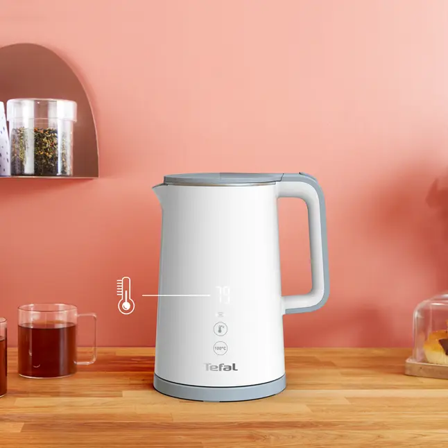 Biało-szary czajnik Tefal na drewnianej powierzchni. Wyświetla temperaturę, z innymi przedmiotami.