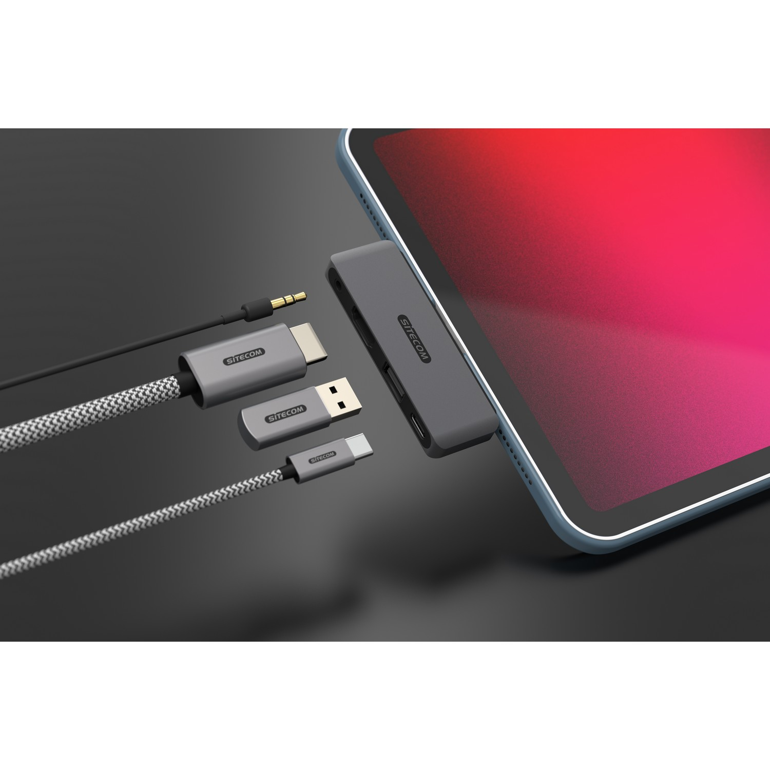 Un iPad connecté à un hub gris avec divers câbles, sur une surface gris foncé.