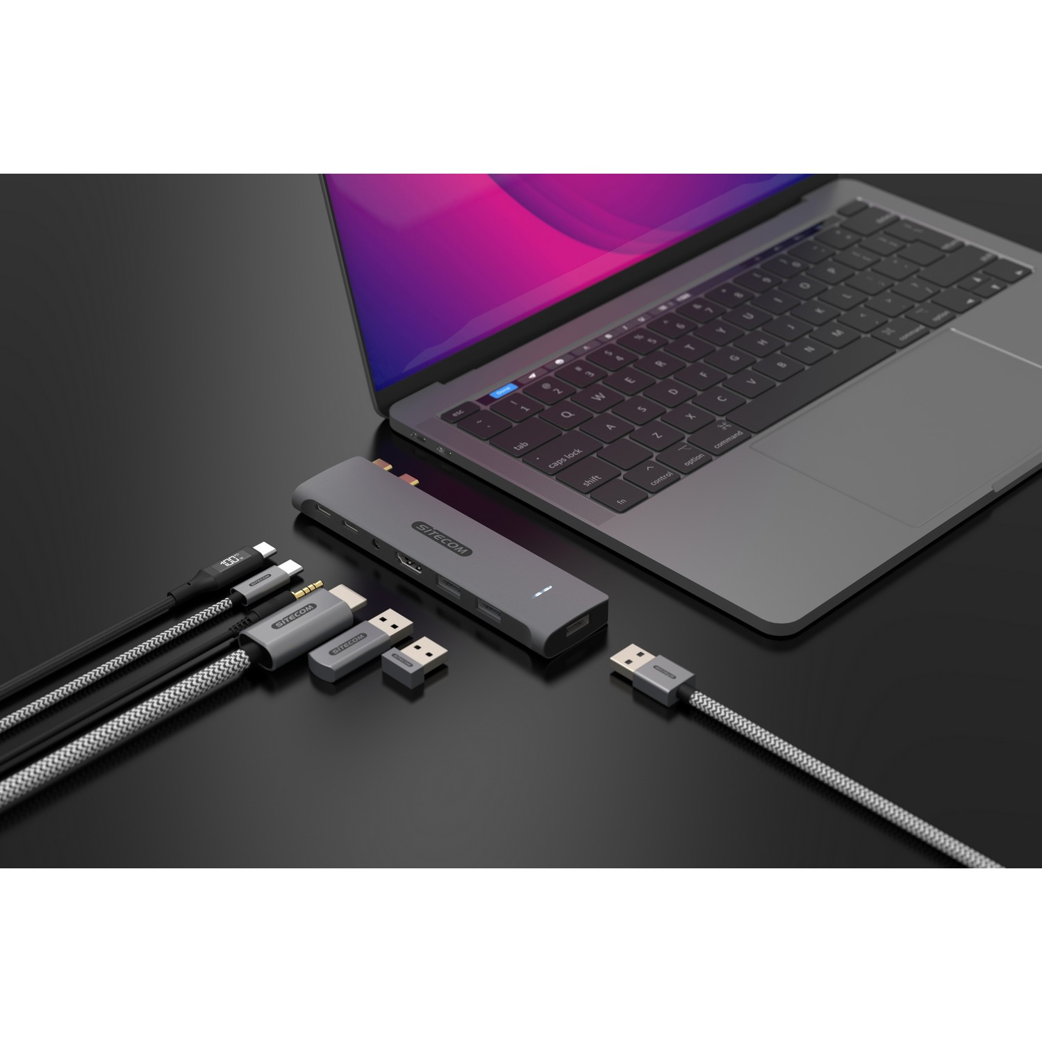 Un ordinateur portable, un hub et plusieurs câbles et adaptateurs sont posés sur une surface sombre. Un câble relie le hub à l'ordinateur portable.