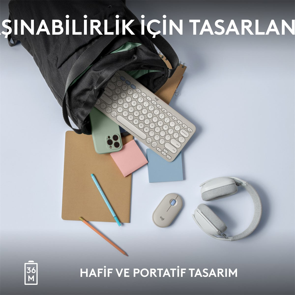 Siyah bir çantadan eşyalar dökülüyor: klavye, fare, telefon ve not defteri açık mavi bir yüzeyde.