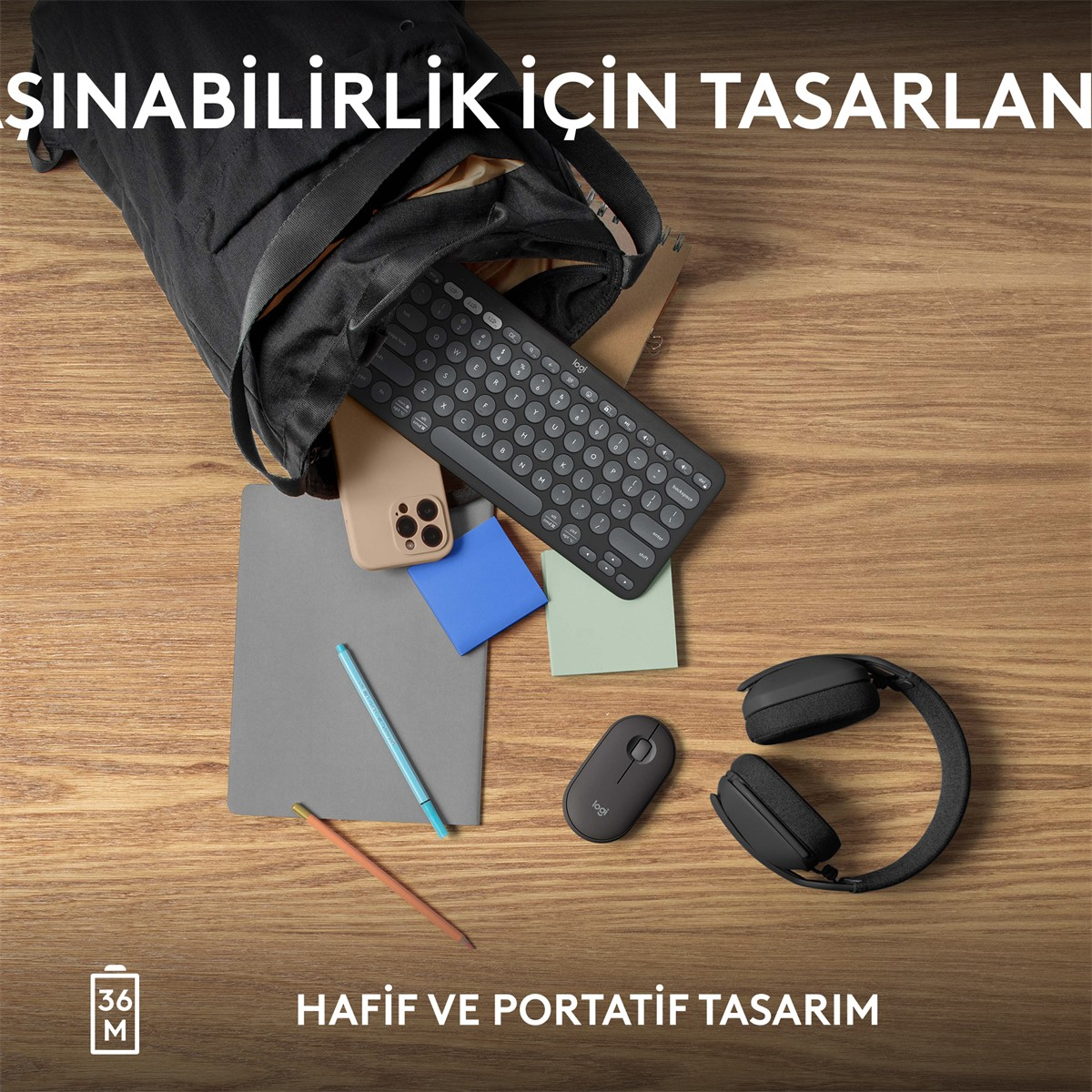 Bir çanta içinde klavye, fare, telefon, not defteri ve kulaklık bulunan bir masa sahnesi.