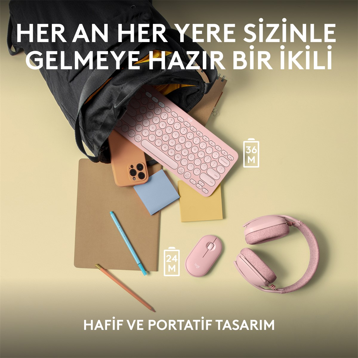 Pembe klavye, telefon, fare ve kulaklık, siyah bir çanta ve not defteri ile sergileniyor.