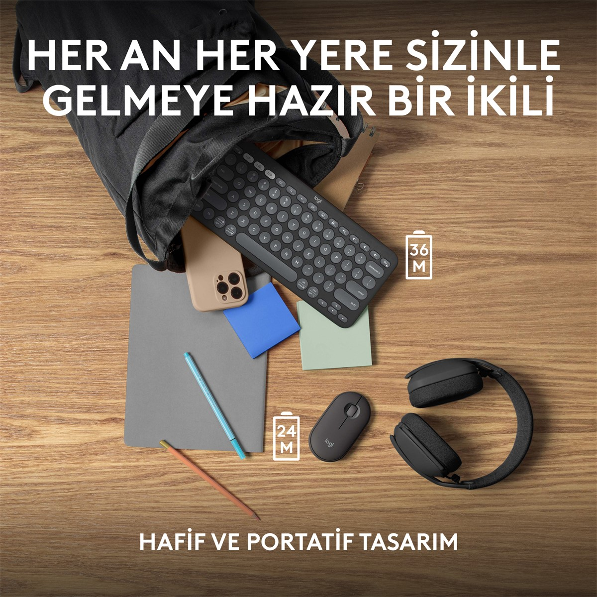 Ahşap bir yüzeyde bir dizüstü bilgisayar, klavye, fare, not defteri, telefon ve kulaklık.