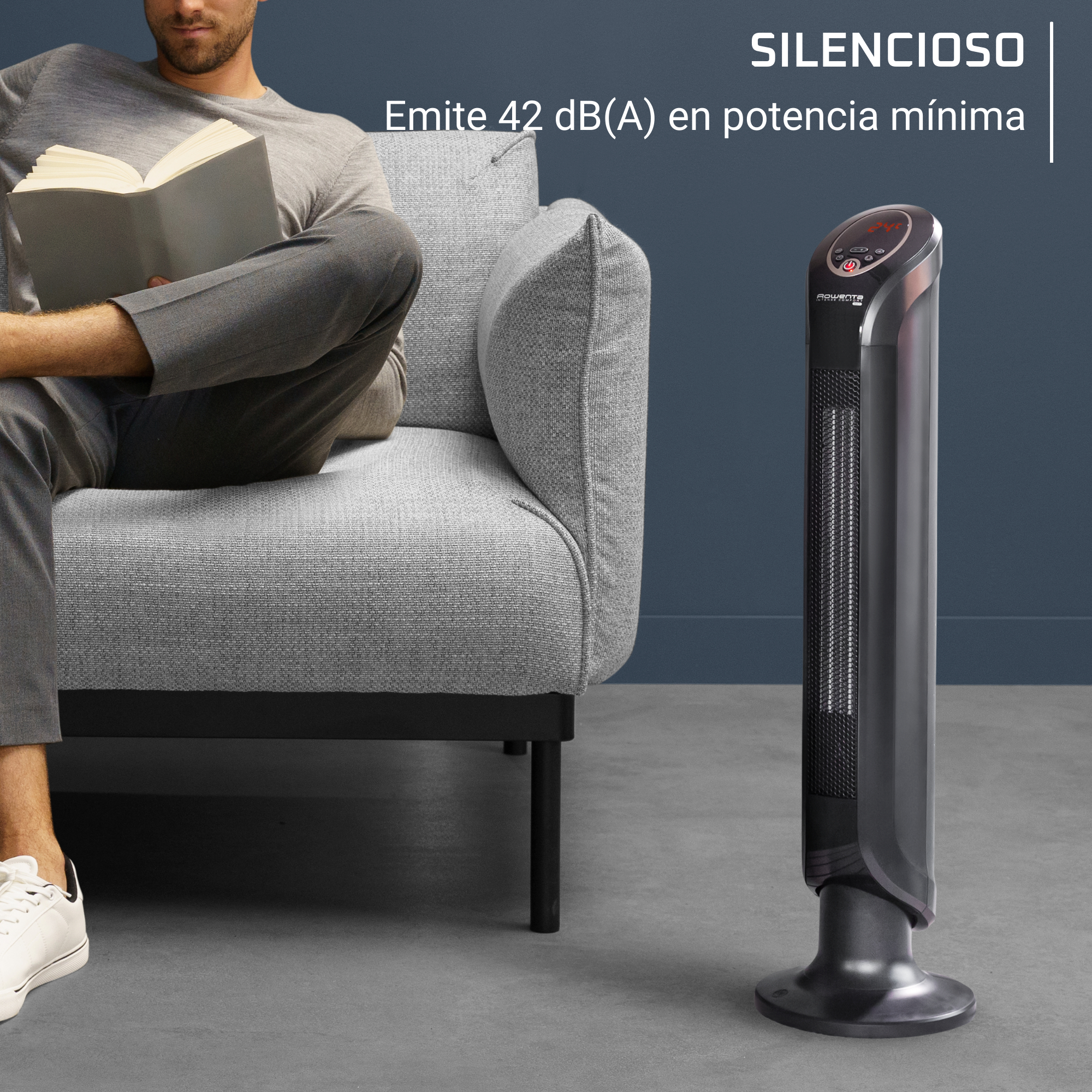 Persona leyendo un libro junto a un calefactor gris sobre suelo gris y pared azul oscura.