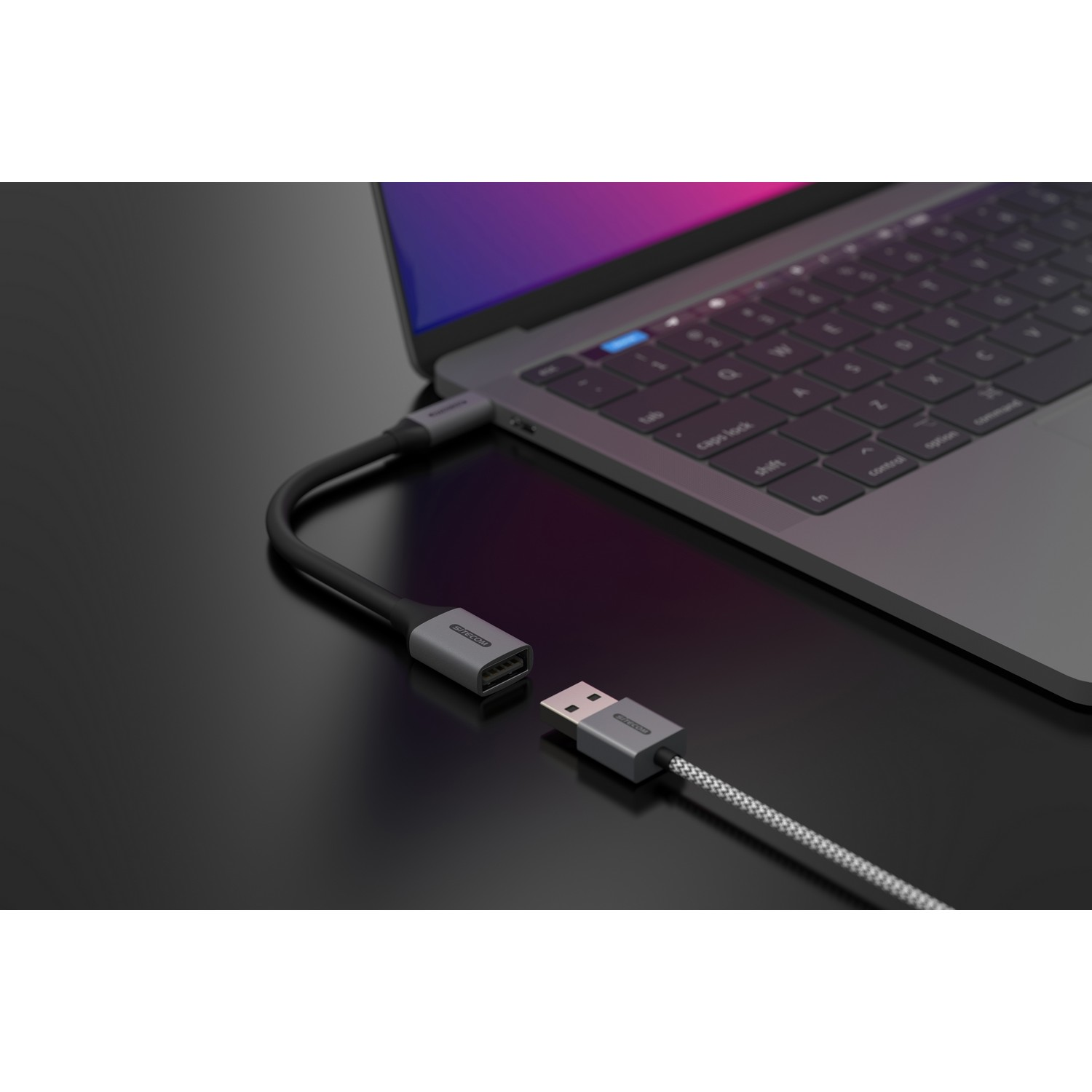 Un câble USB-C vers USB noir et gris connecté à un ordinateur portable sur une surface noire.