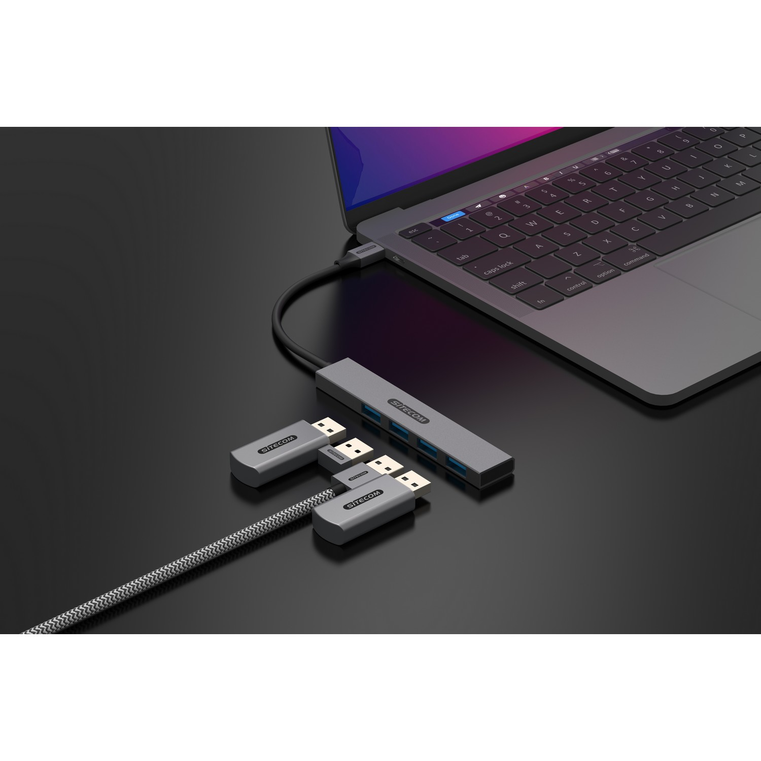 Ordinateur portable connecté à un hub et deux clés USB. Bureau noir. Accessoires argentés.