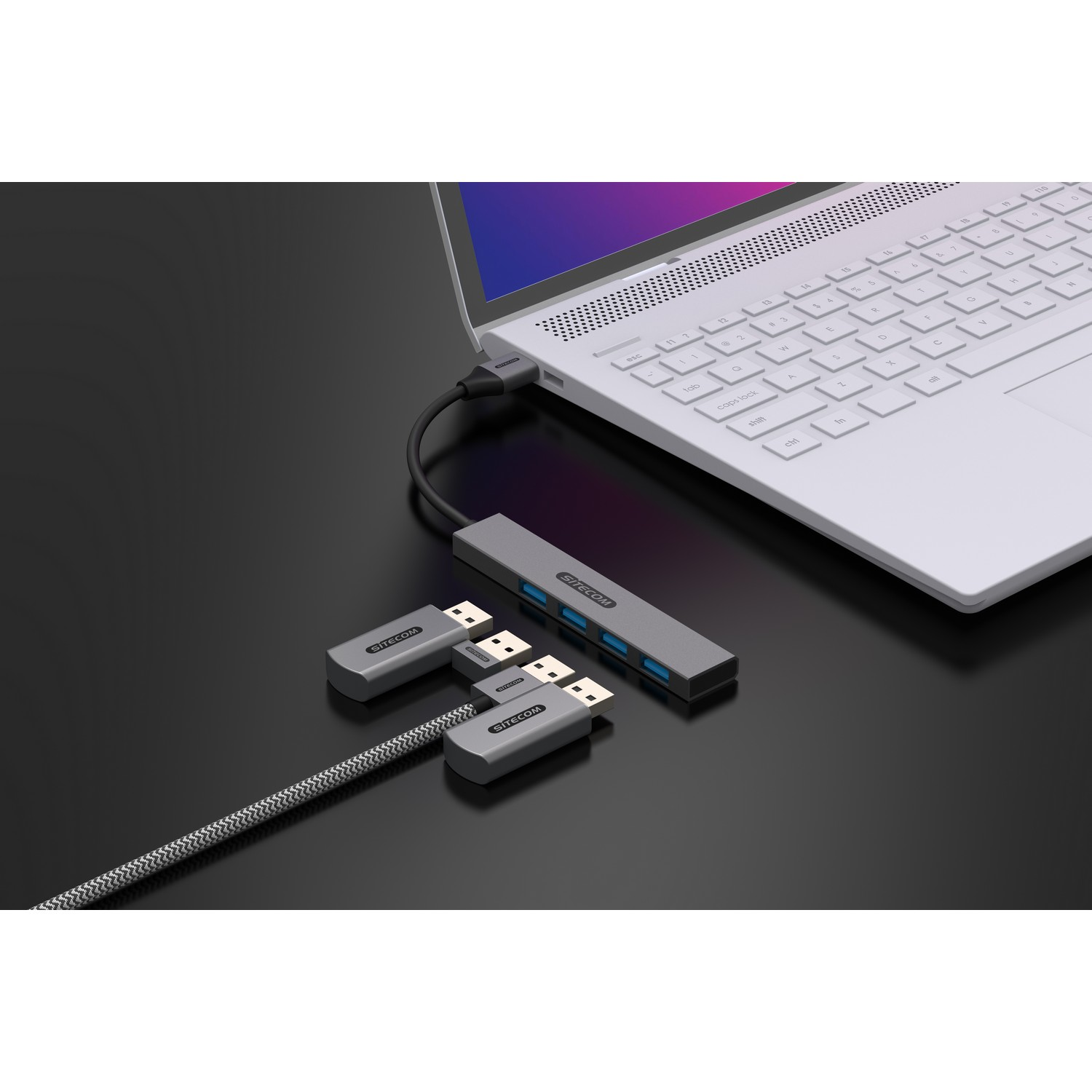 Un ordinateur portable avec un hub USB et deux adaptateurs USB. Le hub est gris, connecté à un ordinateur portable.
