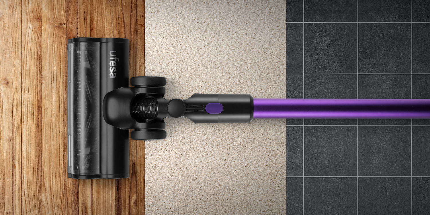 Cabezal de aspiradora sobre madera, alfombra y azulejos, con mango morado.