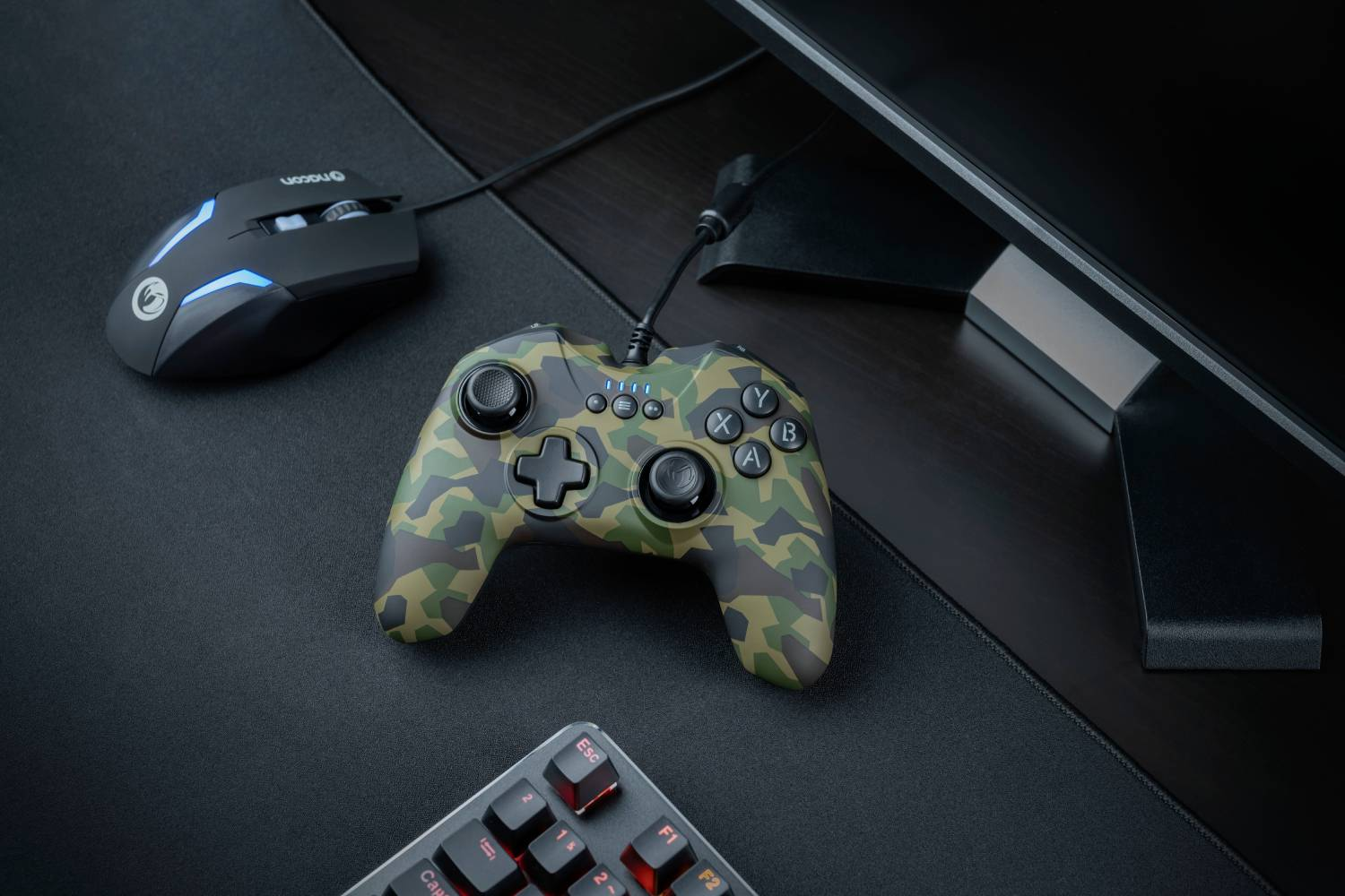 Un controlador de camuflaje, un ratón negro y un teclado sobre una superficie negra.