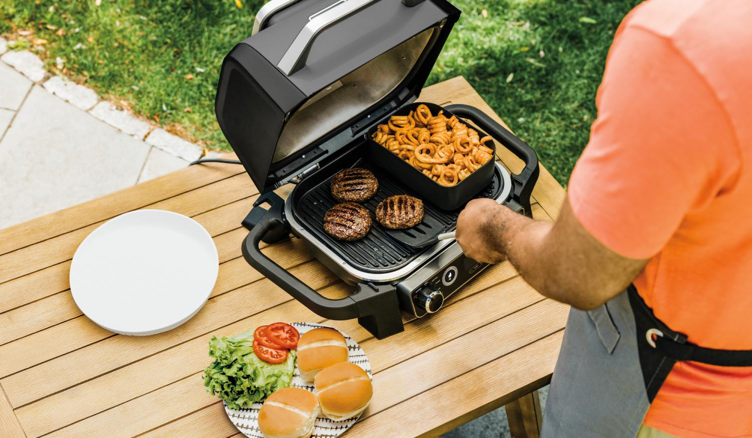 Un hombre a la parrilla hamburguesas y patatas fritas rizadas al aire libre.