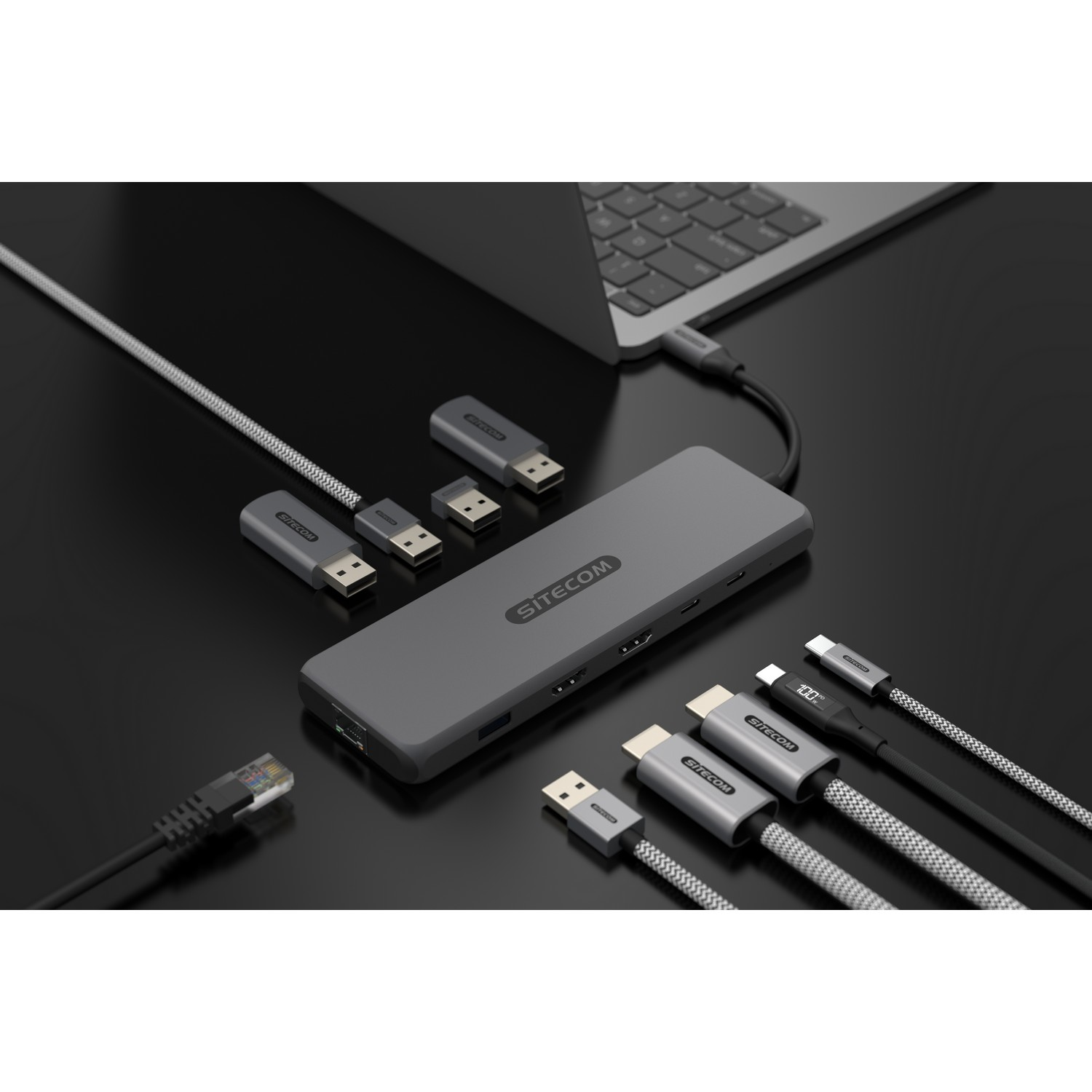 Un hub SITECOM gris avec plusieurs ports, des câbles USB-C et Ethernet. Ordinateur portable sur une surface sombre.