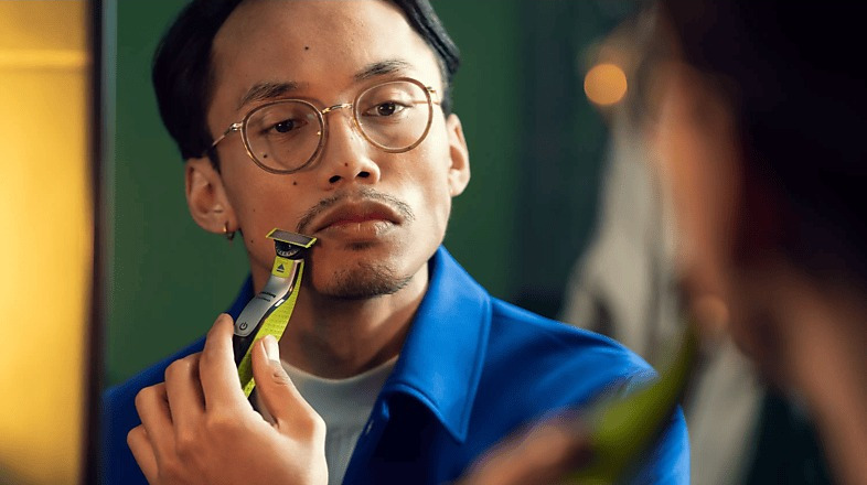 Homme avec des lunettes se rase le visage avec un rasoir électrique Philips OneBlade vert et argenté.