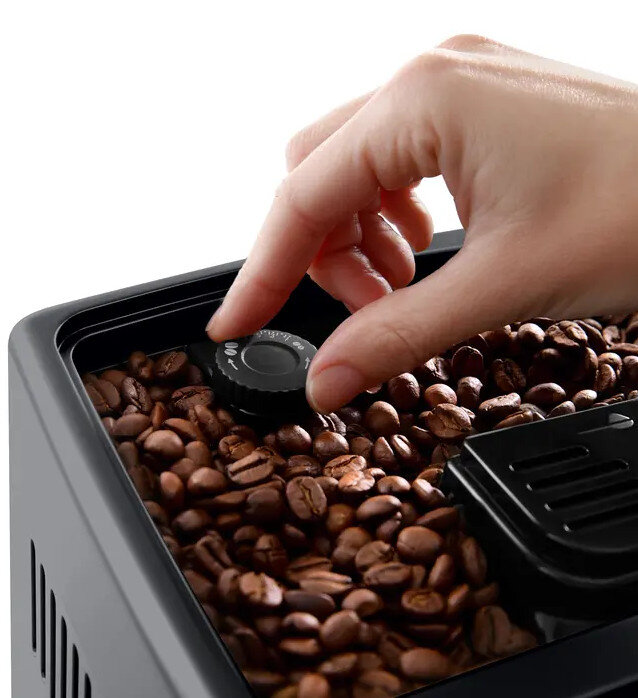 Ręka obracająca pokrętło w ekspresie do kawy wypełnionym ziarnami kawy.