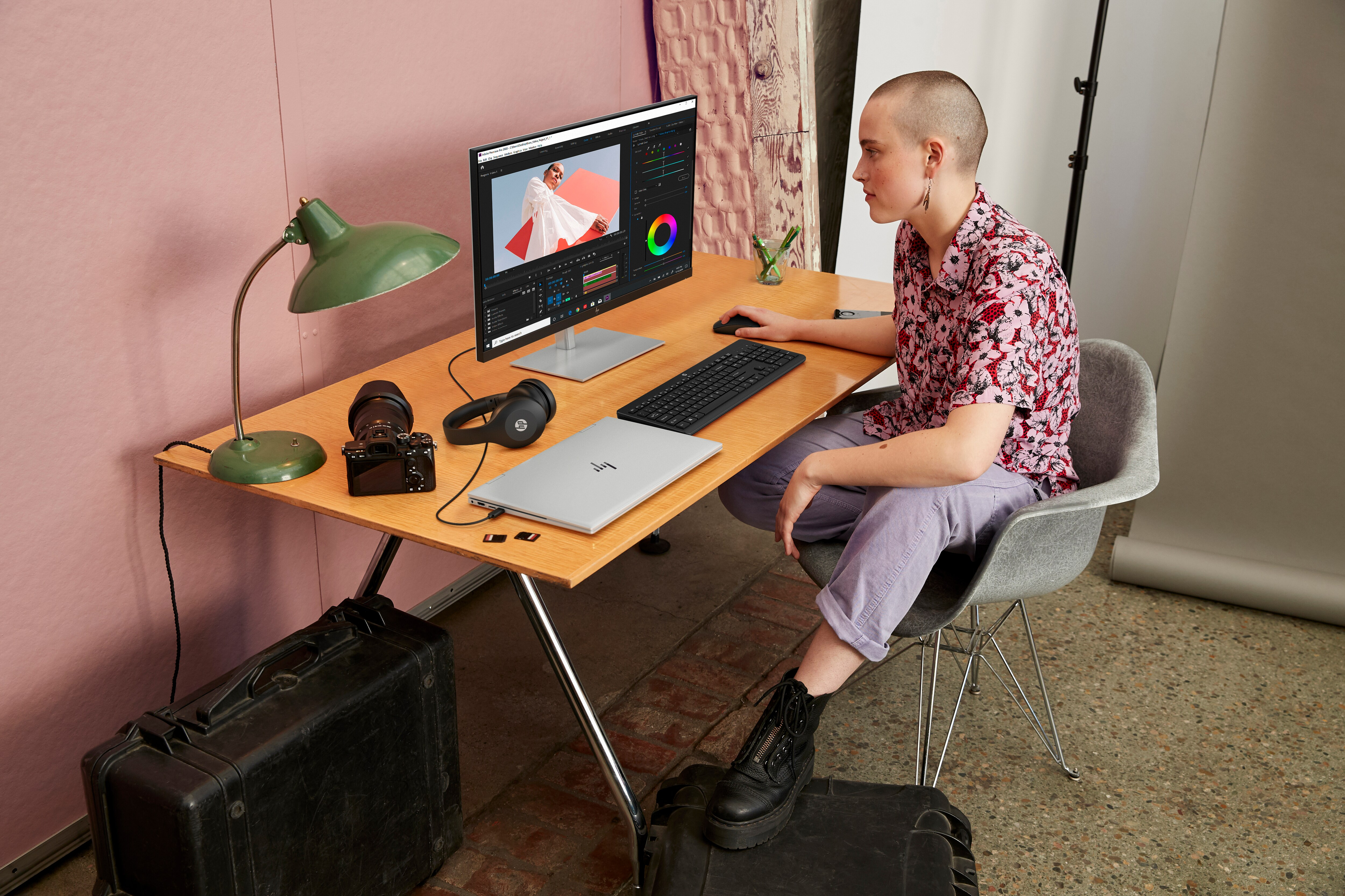 Frau arbeitet an einem Schreibtisch und bearbeitet Fotos, mit Monitor, Kamera und Laptop.