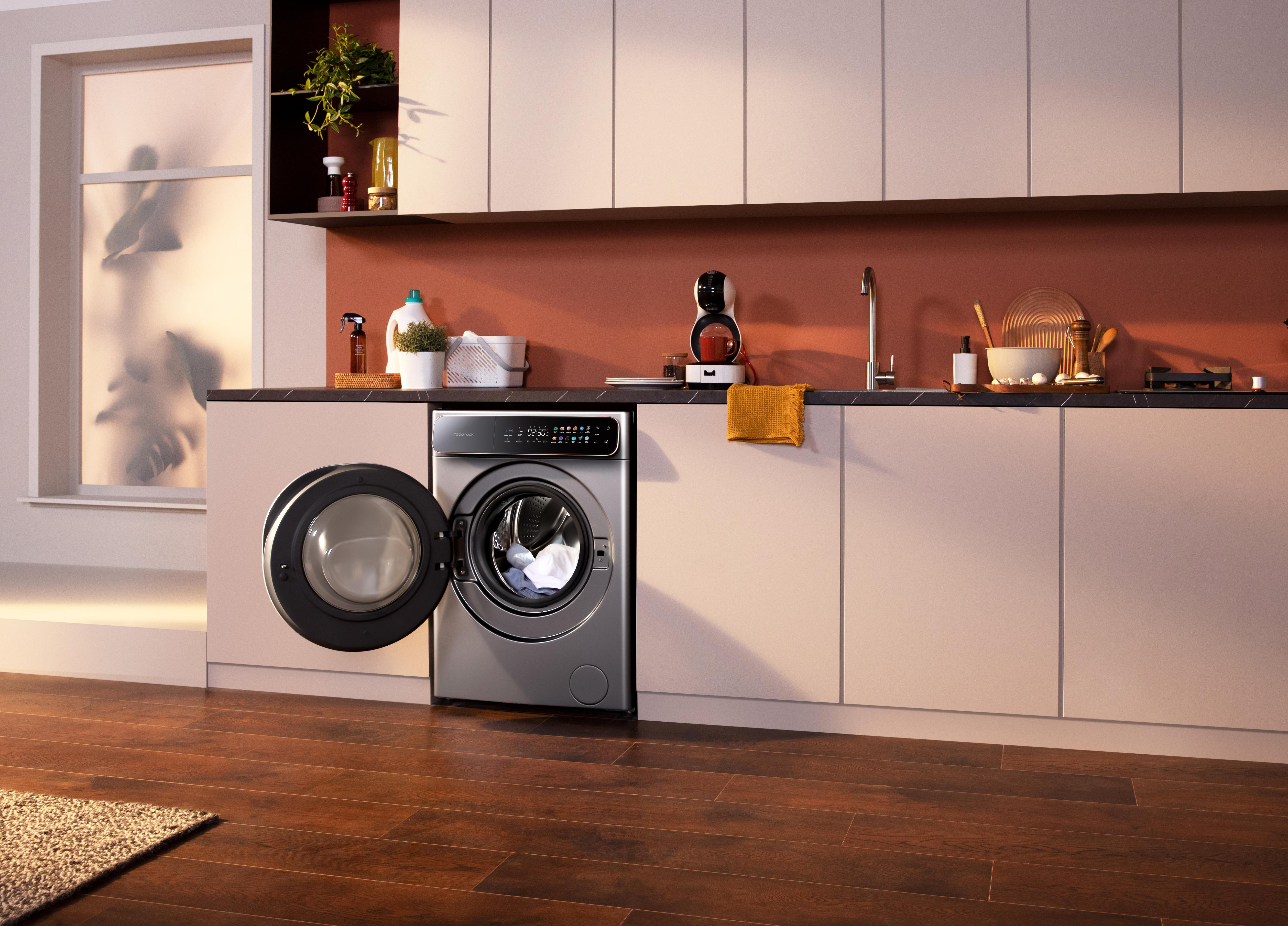 Eine moderne Küche mit Waschmaschine. Offene Tür zeigt Kleidung. Schränke und Arbeitsplatte mit Geräten und Dekor.