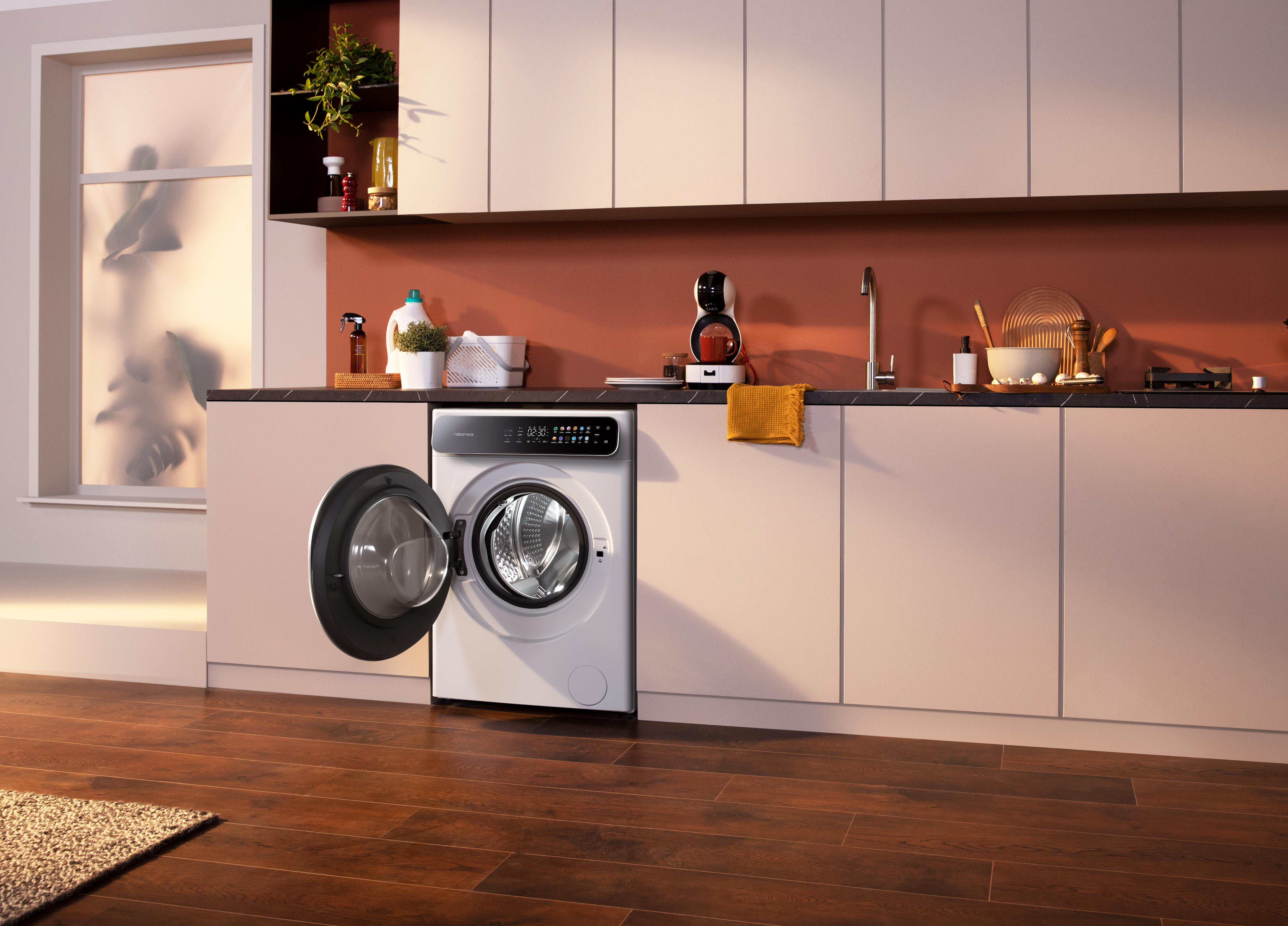 Moderne Küche mit Waschmaschine. Die Tür der Maschine ist offen. Schränke, ein Fenster und Geräte sind ebenfalls sichtbar.