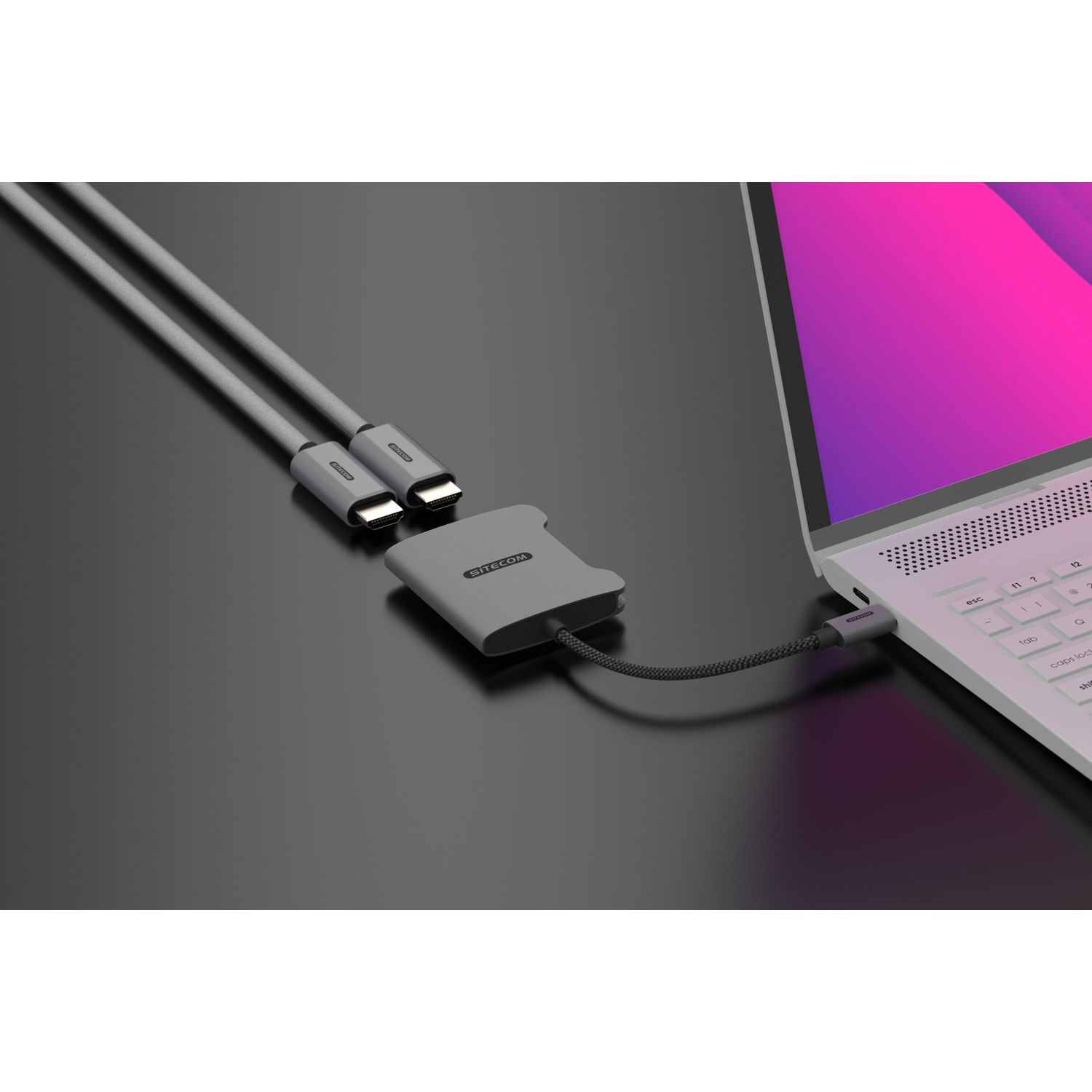 Un hub gris connecté à un ordinateur portable avec un câble USB-C, sur fond sombre.