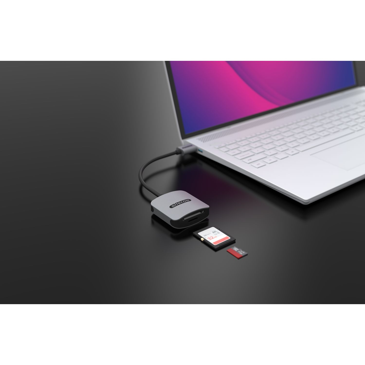 Un lecteur de carte argenté connecté à un ordinateur portable, avec des cartes SD, sur une table noire.