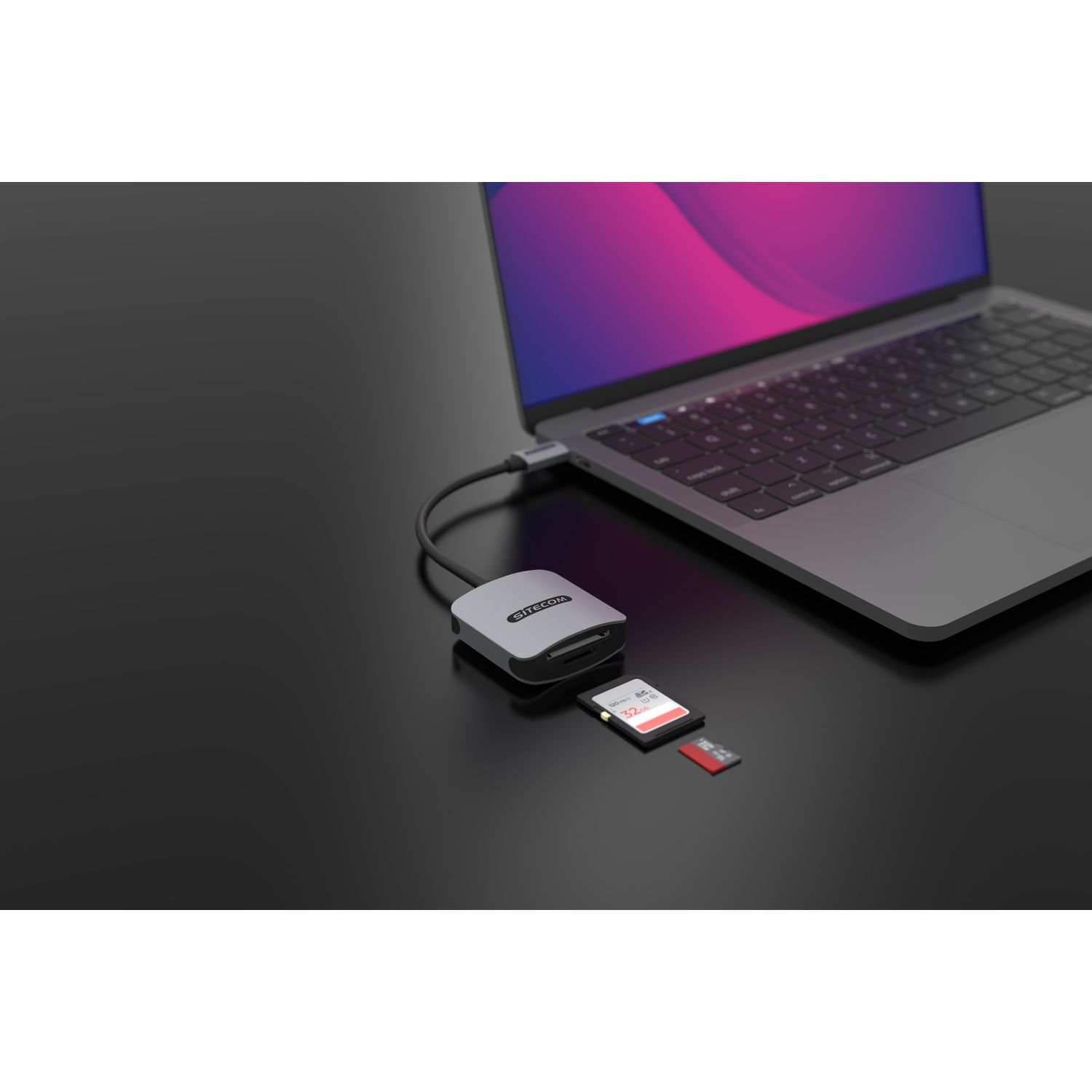 A laptop connected to a grey card reader with two SD cards inserted, on a black surface.