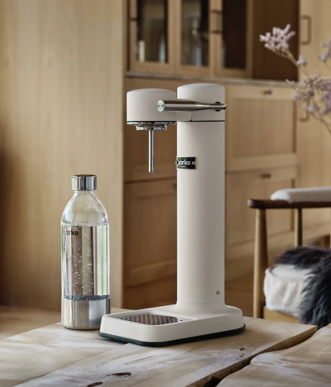 Ein Soda-Maker, eine Glasflasche und eine Wasserflasche stehen auf einem Holztisch.