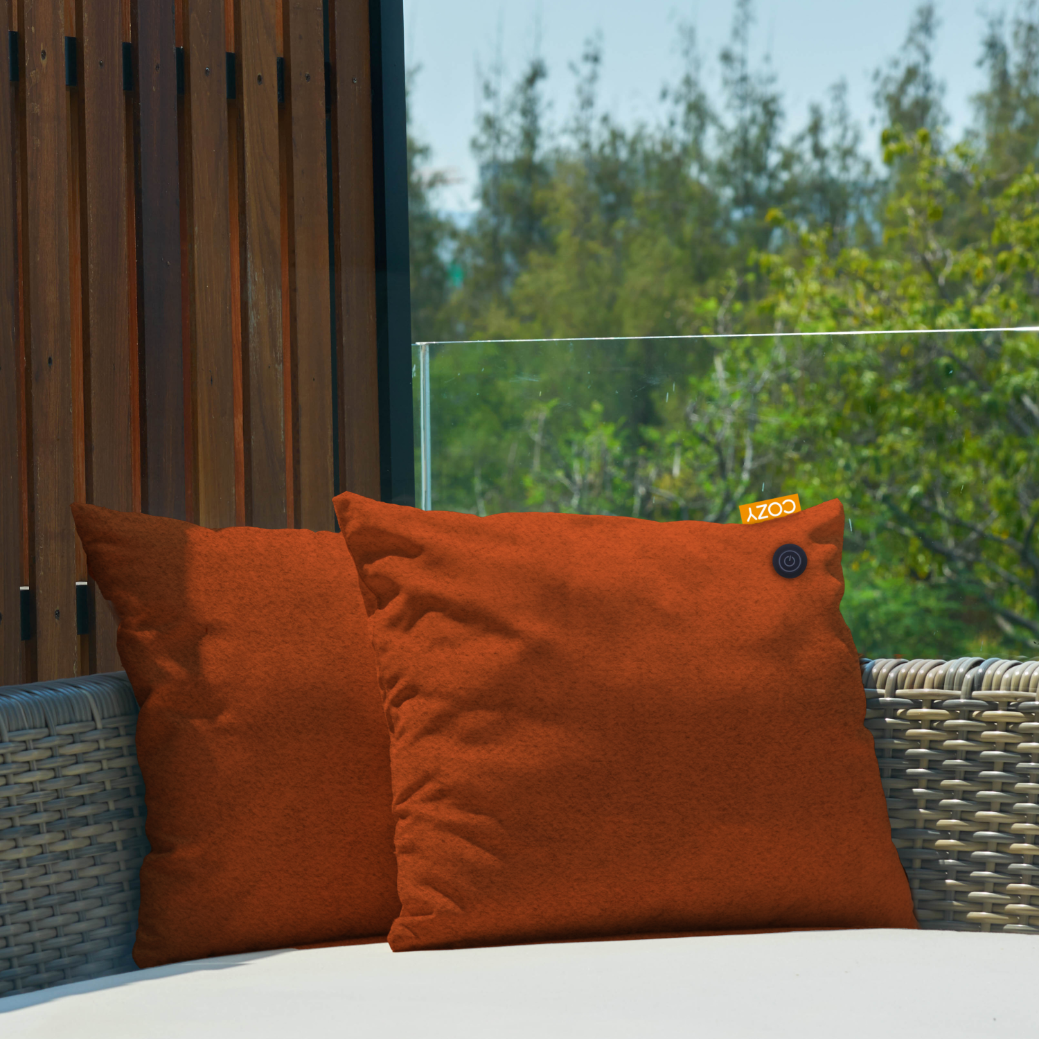 Two orange square pillows on a white surface with a COZY tag and power button.