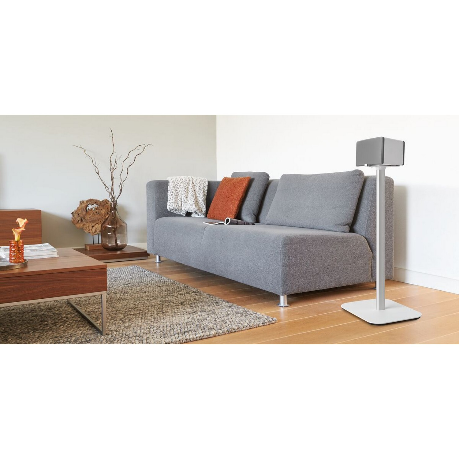 Een moderne woonkamer met een grijze bank, houten salontafel en een luidspreker op een standaard. Neutrale tinten.