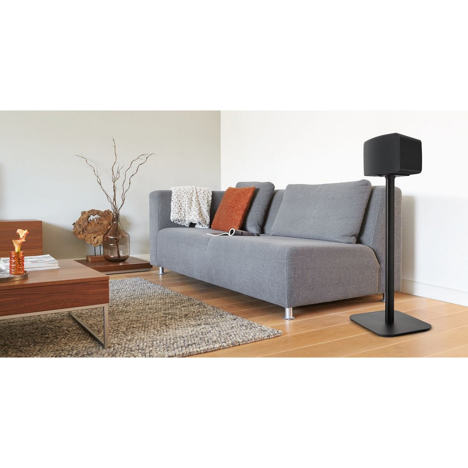 Moderne woonkamer met grijze bank, salontafel, luidspreker op standaard en decoraties.
