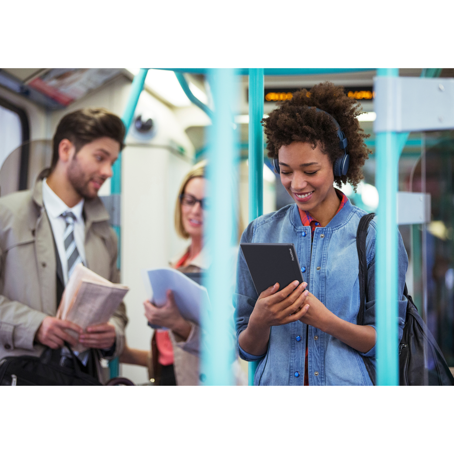 Vrouw in een trein die een tablet vasthoudt, met twee mannen die naar haar kijken, één leest een krant.