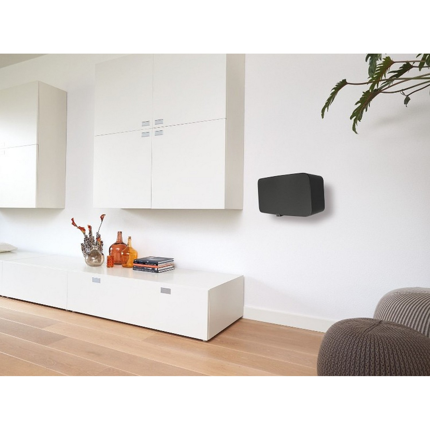 Enceinte noire murale sur un mur blanc. Un meuble blanc est en dessous.