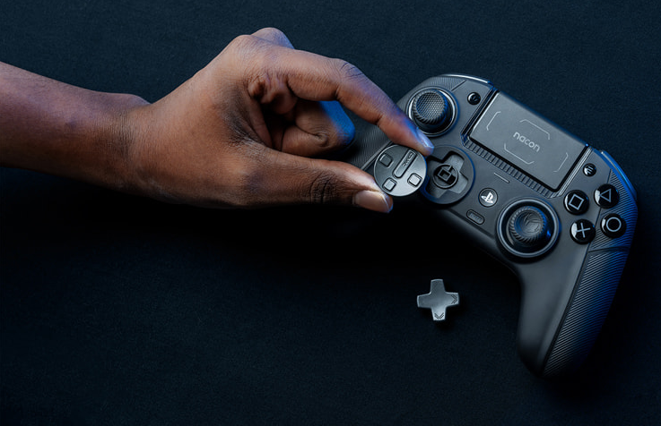 Eine Hand hält eine Taste eines schwarzen Gamecontrollers. Der Controller liegt auf einer schwarzen Oberfläche.