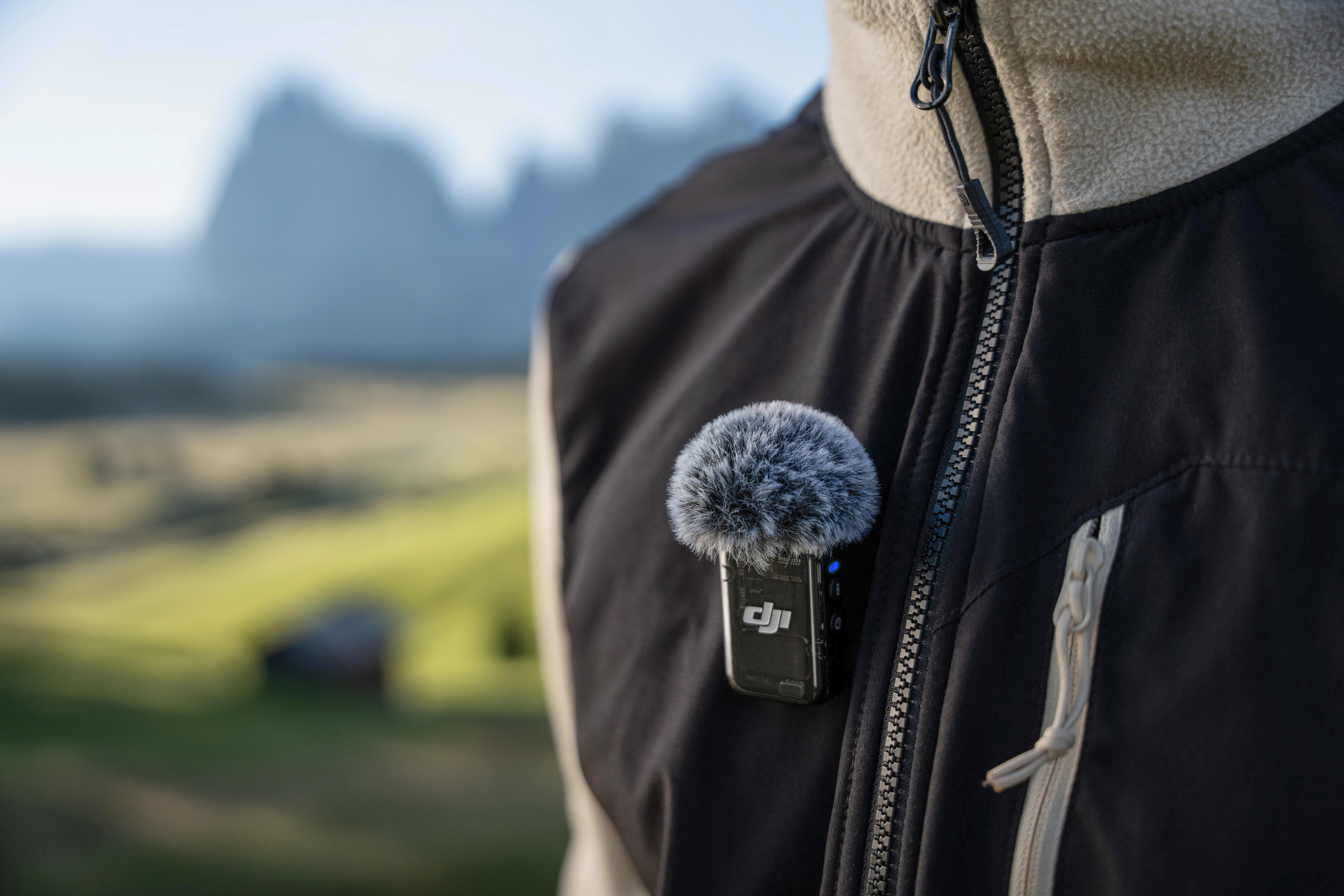 Una persona indossa una giacca con un piccolo microfono, con montagne sullo sfondo.