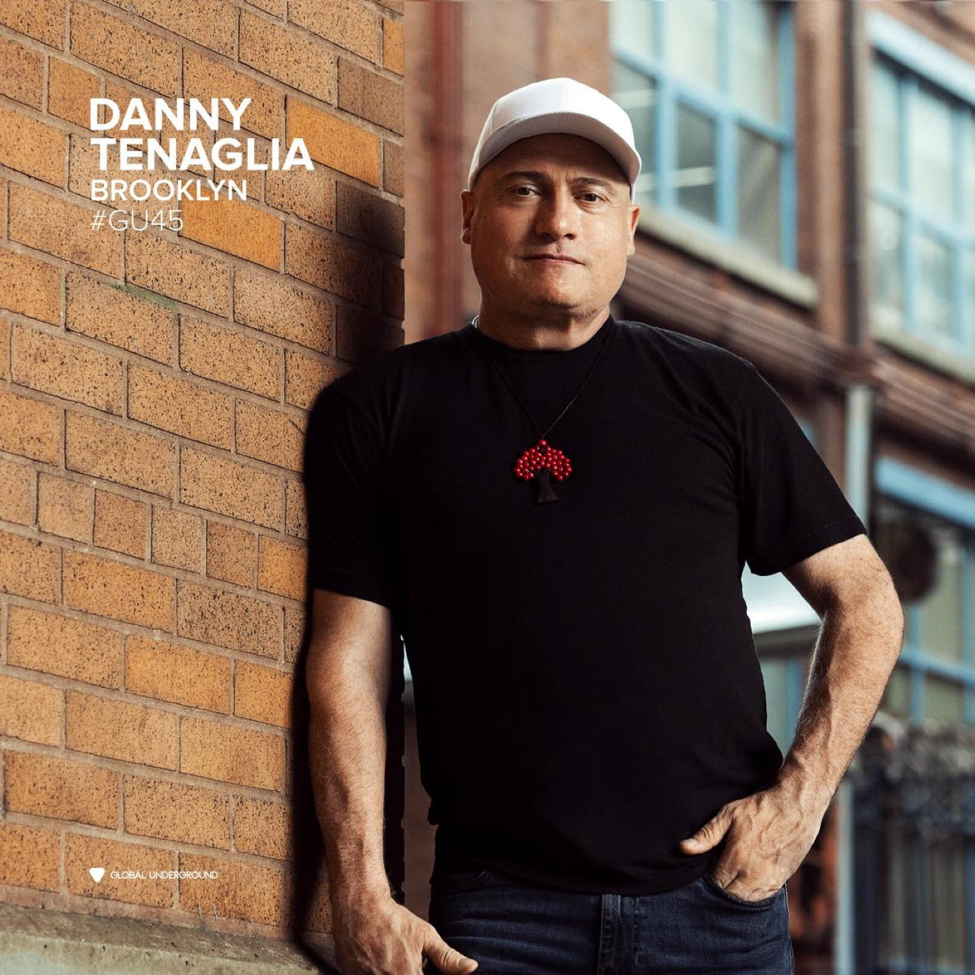 Mann lehnt an Ziegelmauer, trägt weiße Kappe, schwarzes Hemd. Text: Danny Tenaglia, Brooklyn.