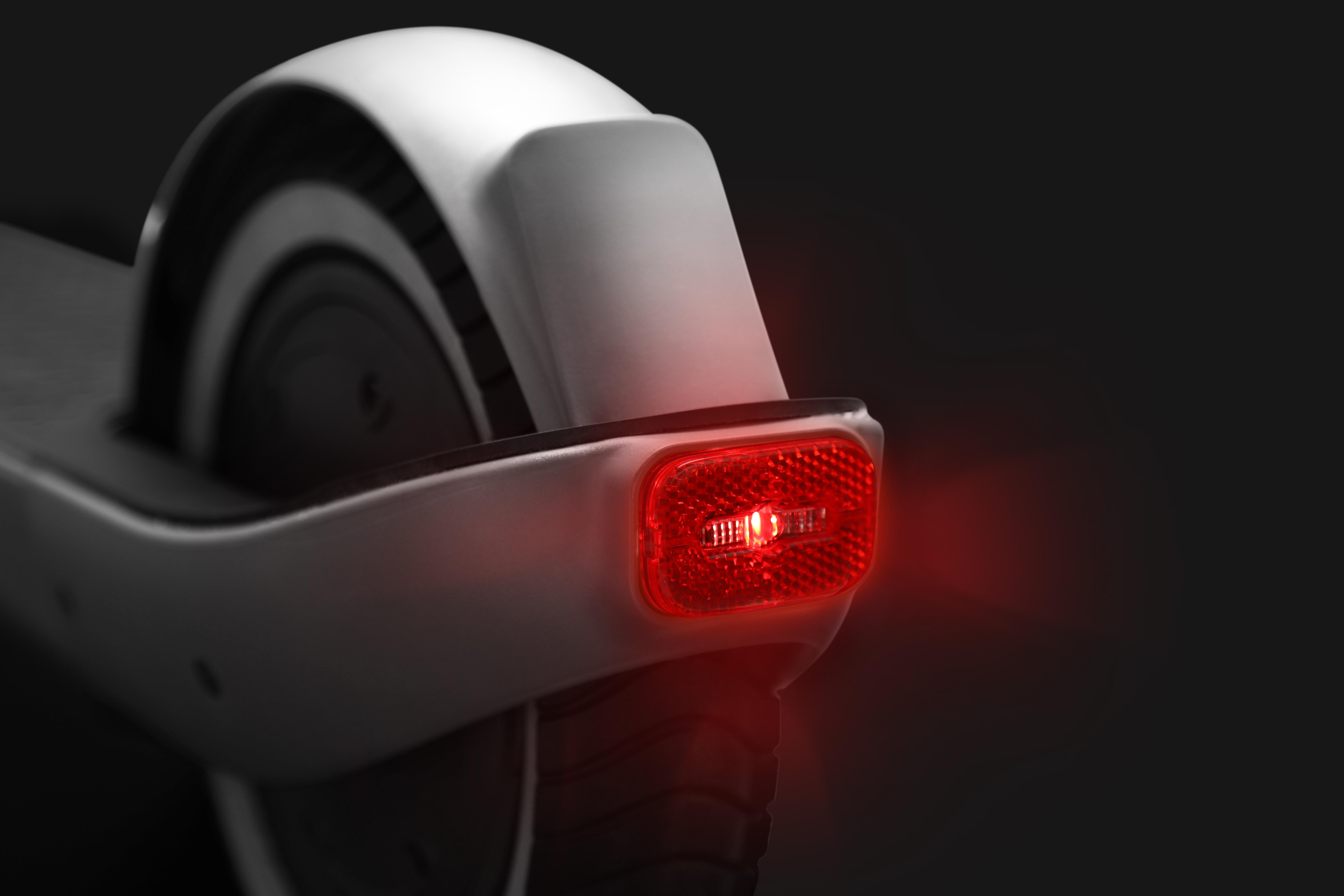 Rückseite eines weißen Elektrorollers mit rotem Reflektorlicht vor dunklem Hintergrund.