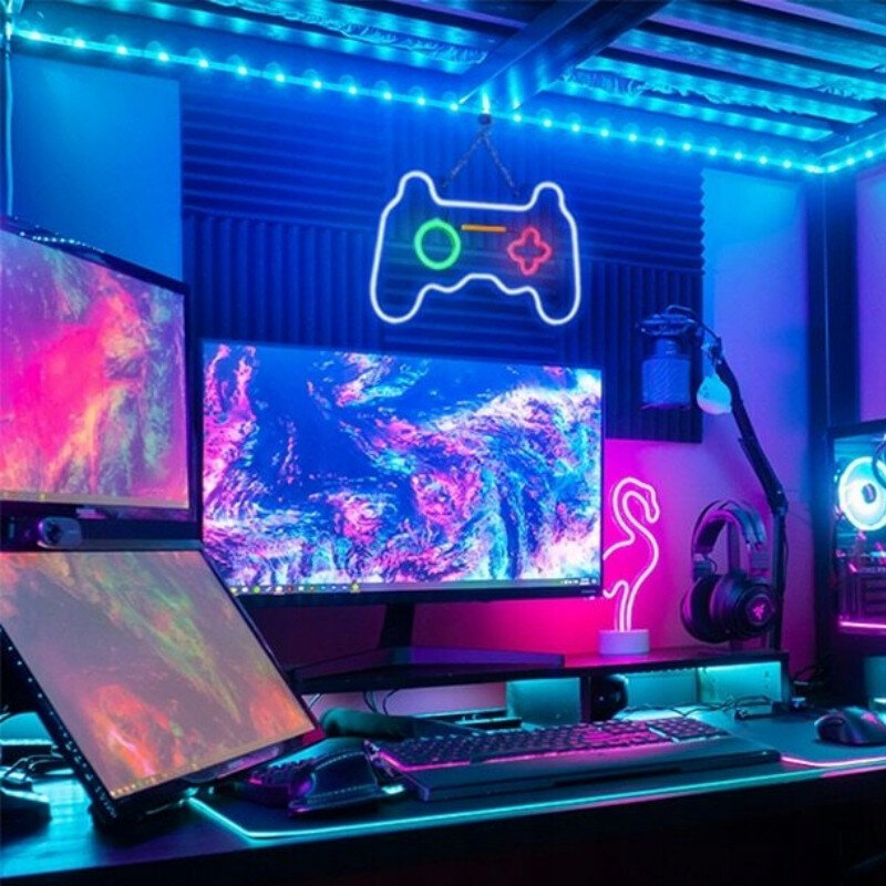 Konfiguracja do gier z wieloma monitorami, neonami, znakiem kontrolera i klawiaturą na biurku. Ciemny pokój.