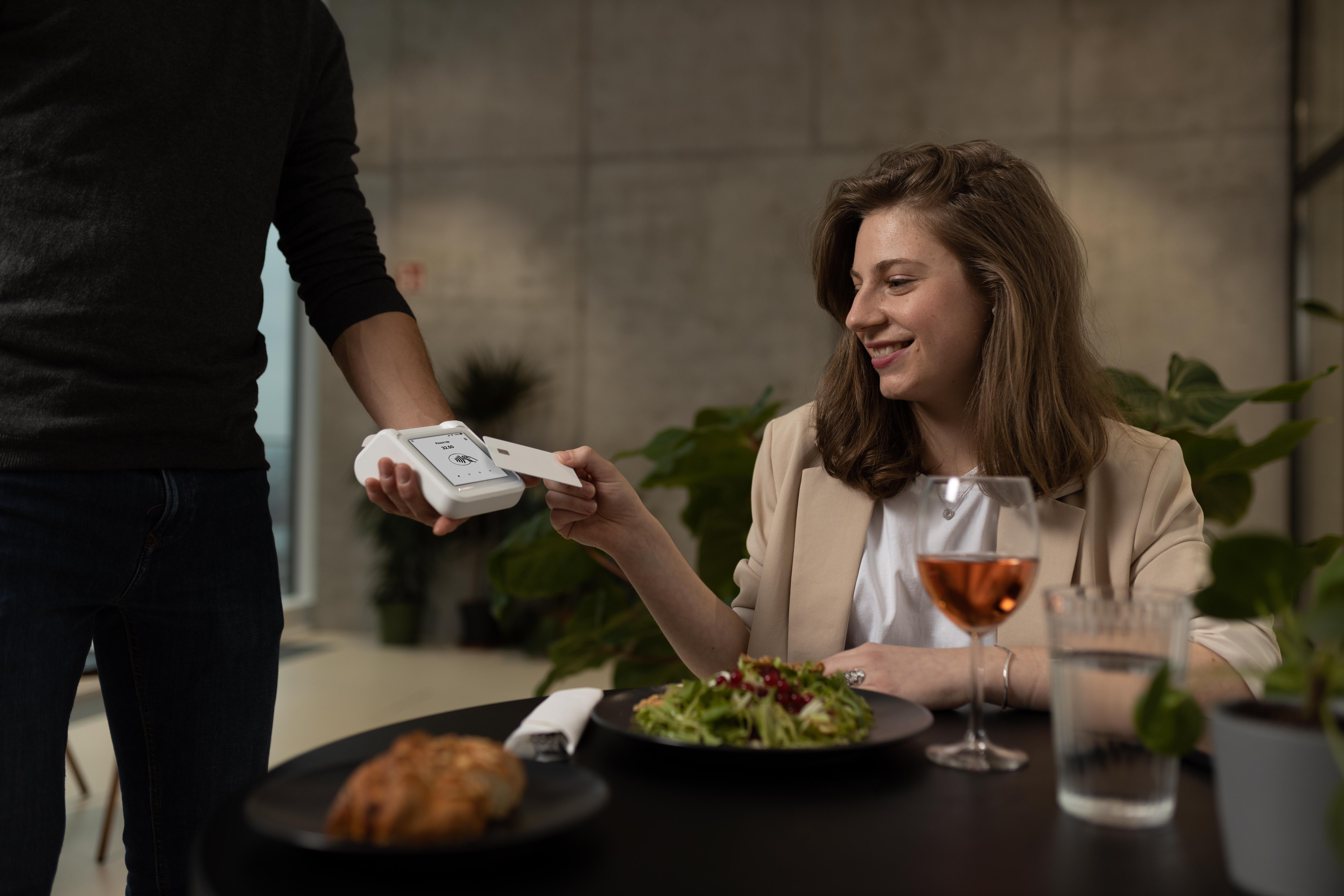 Eine Frau bezahlt mit Kreditkarte in einem Restaurant. Ein Mann bedient das Kartenlesegerät.