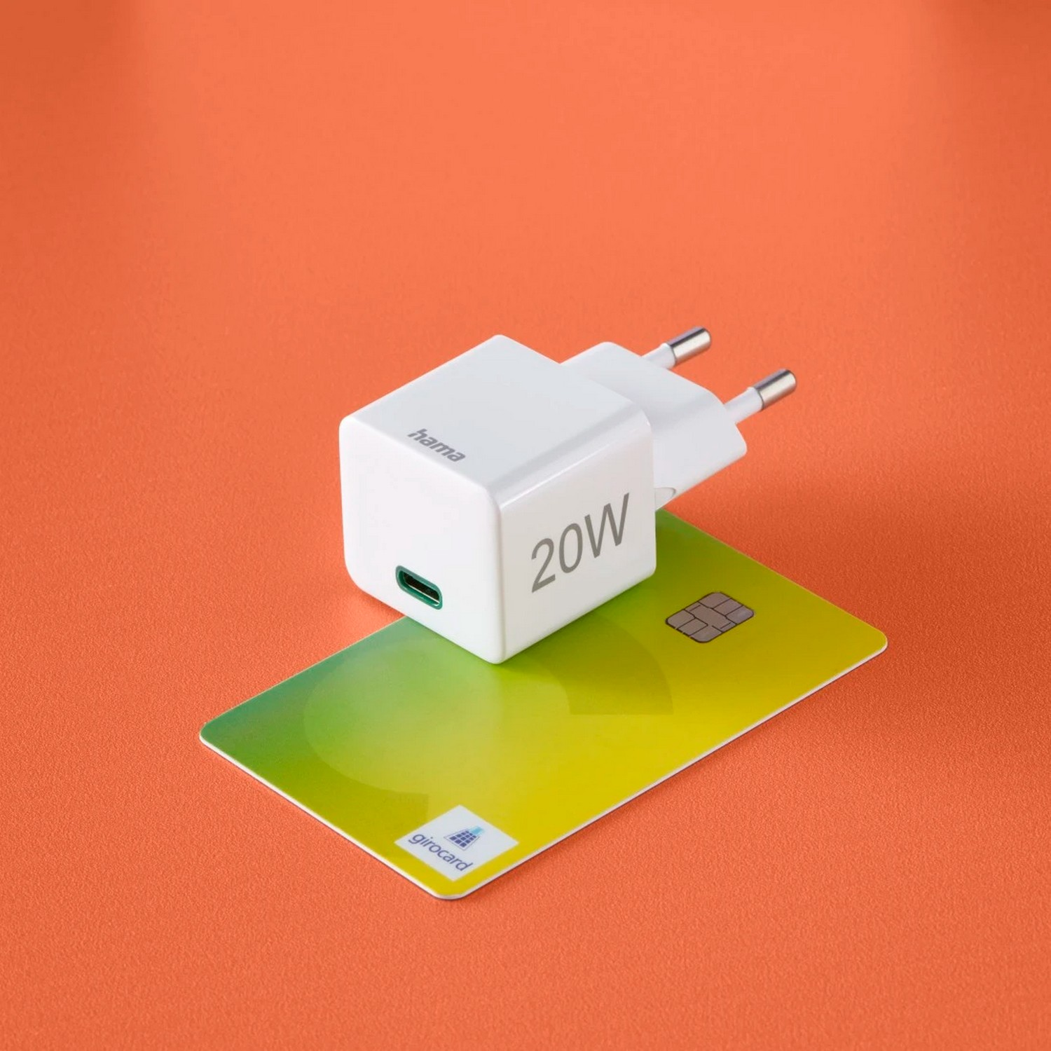 Witte 20W-oplader met een USB-C-poort en stekker, op een oranje achtergrond en een creditcard.