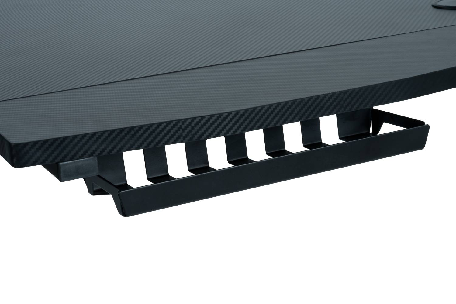 Un escritorio negro con textura de fibra de carbono. Hay una bandeja para cables negra.